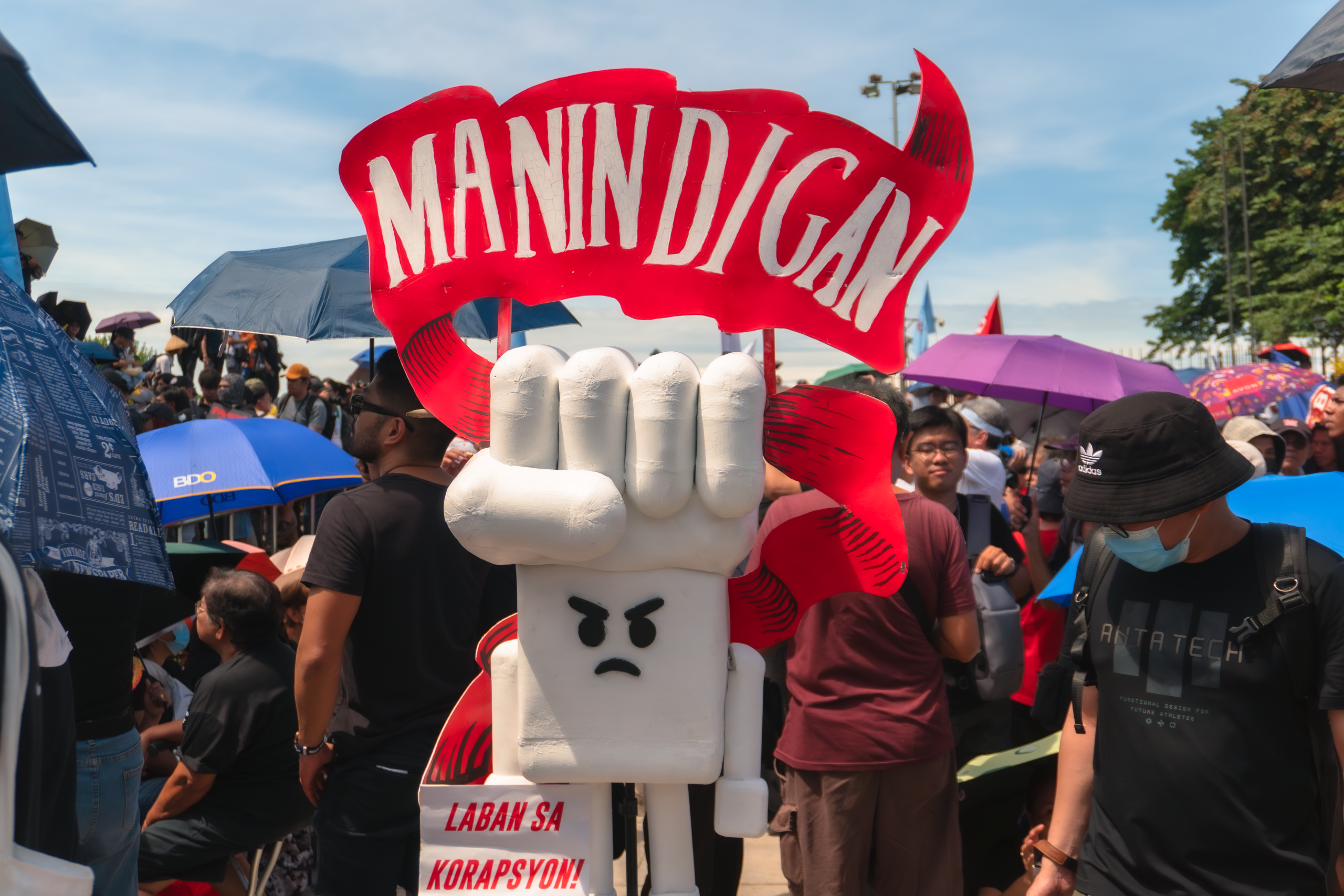 Crowd rallying against corruption in a public square, holding signs and calling for accountability