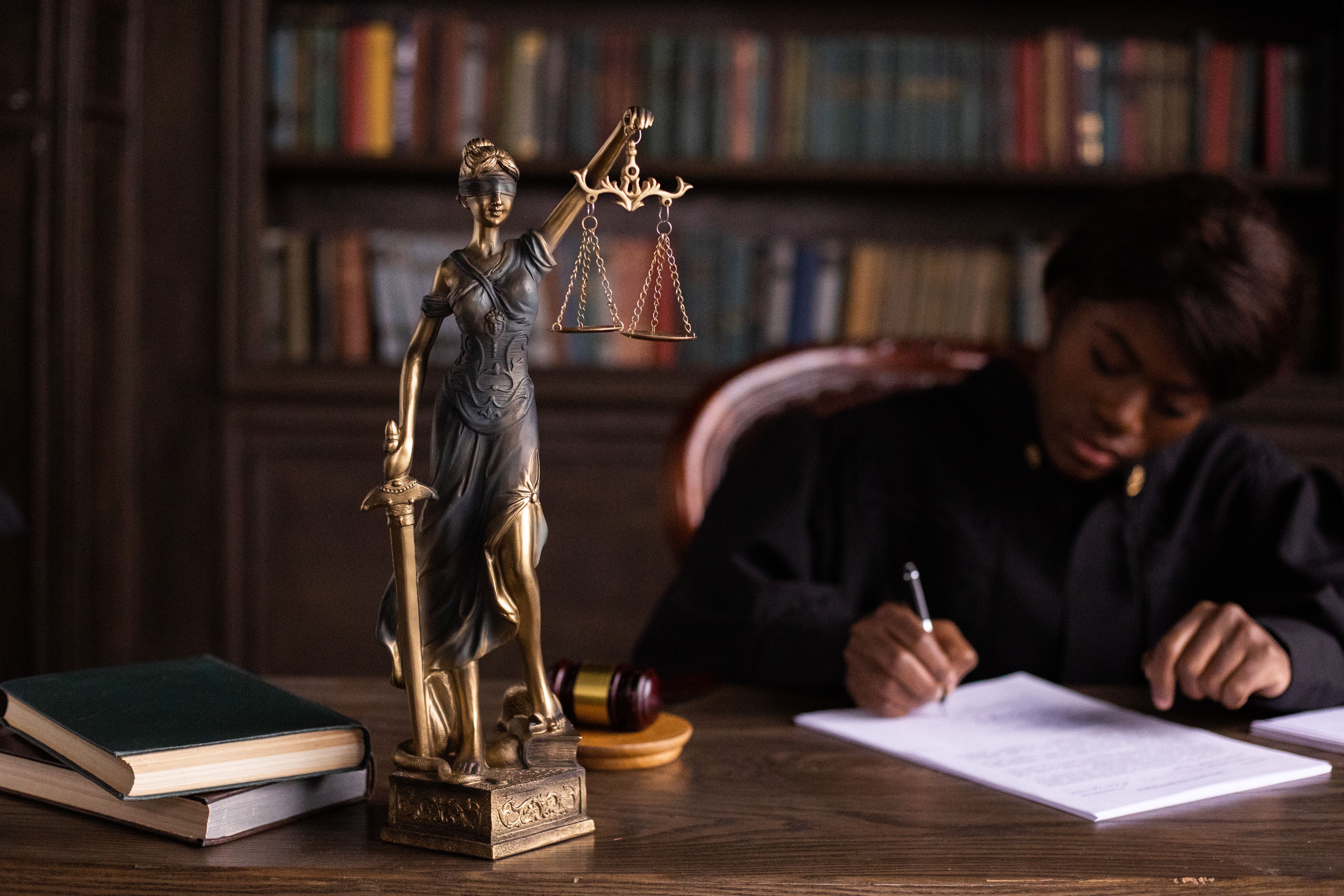 Judge writing at a desk beside a Lady Justice statue, symbolizing anti-corruption law and accountability