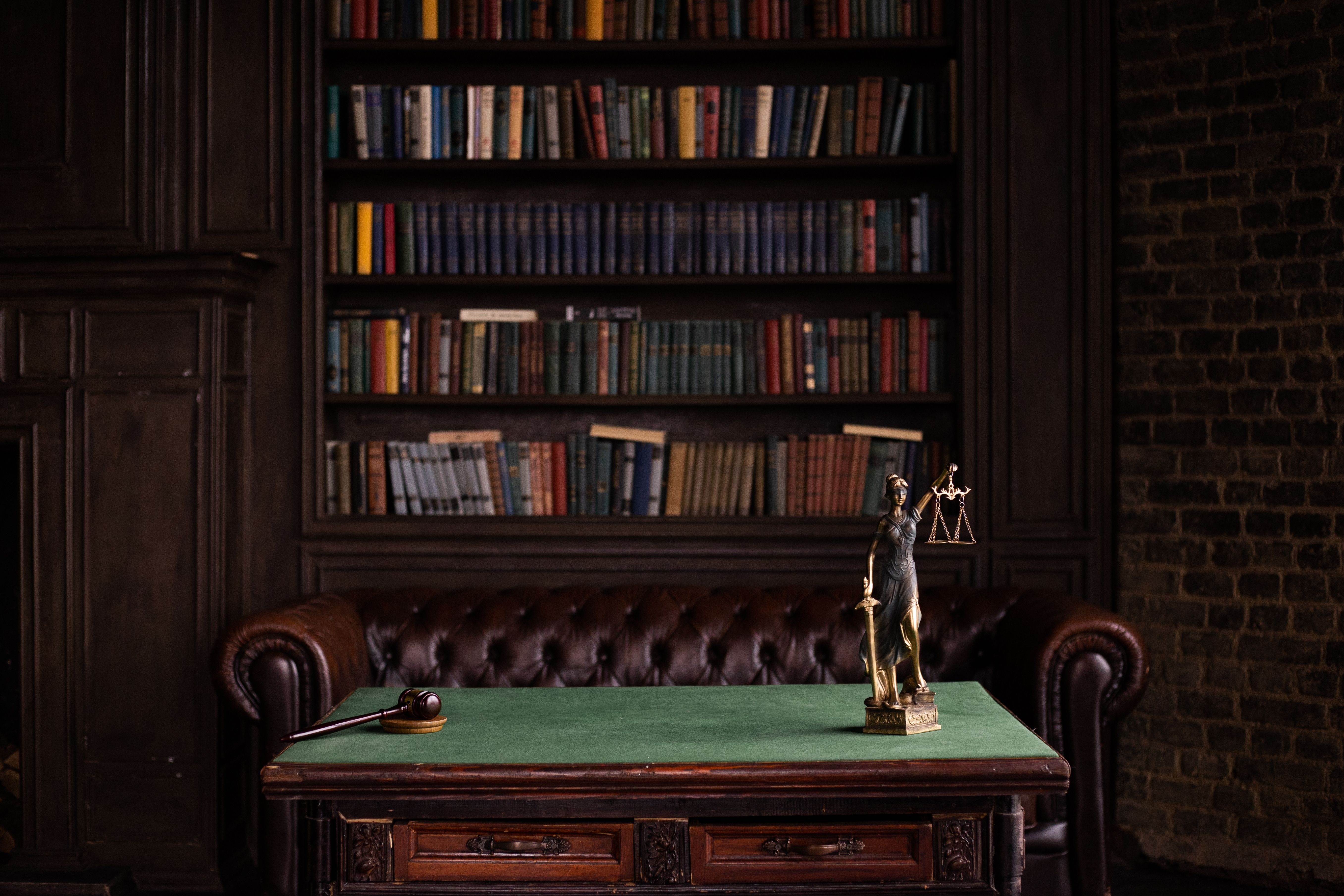Classic study room with shelves of books, a gavel, and a Lady Justice figurine on a green table