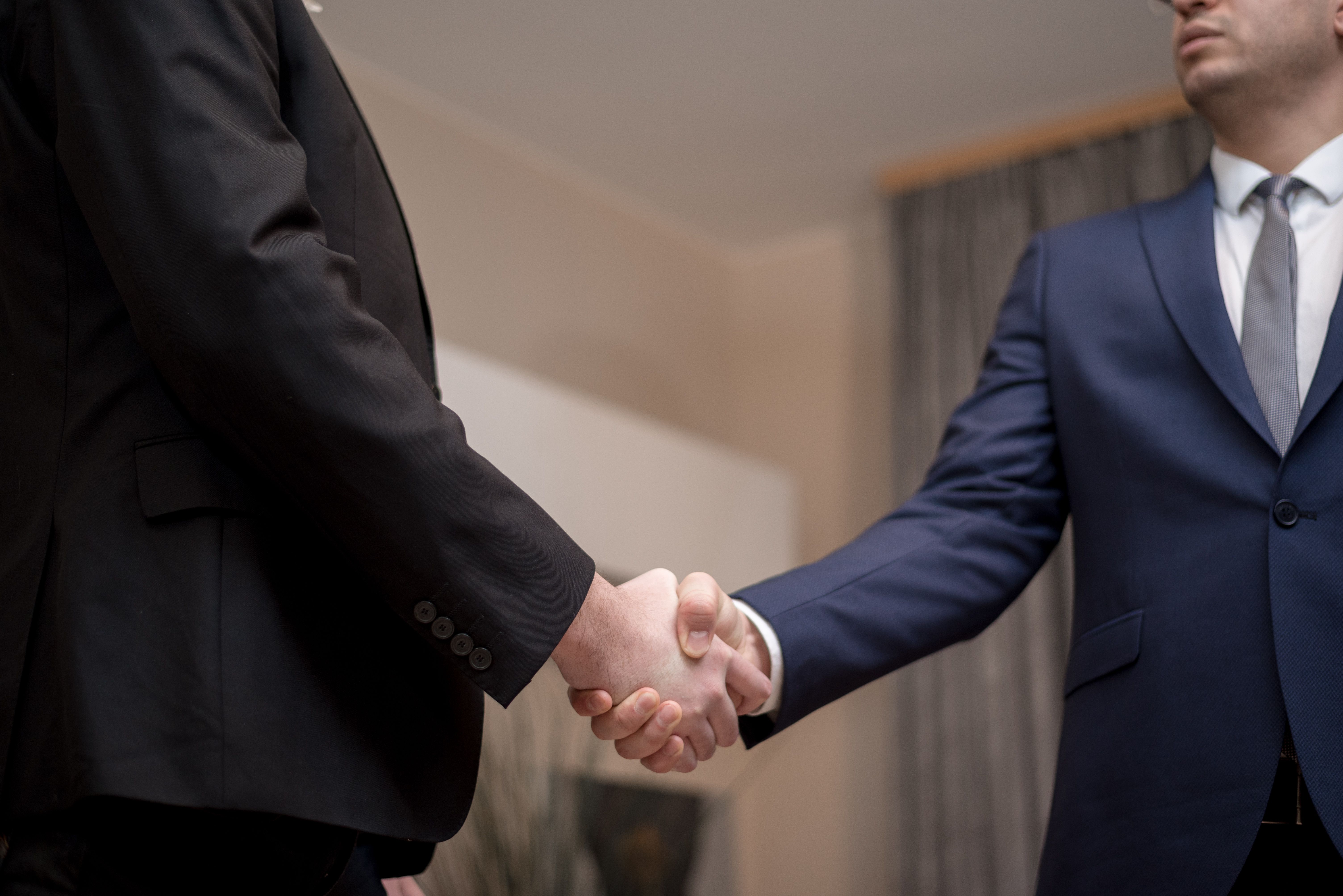 Two businessmen in suits shaking hands, illustrating backroom deals and political alliances