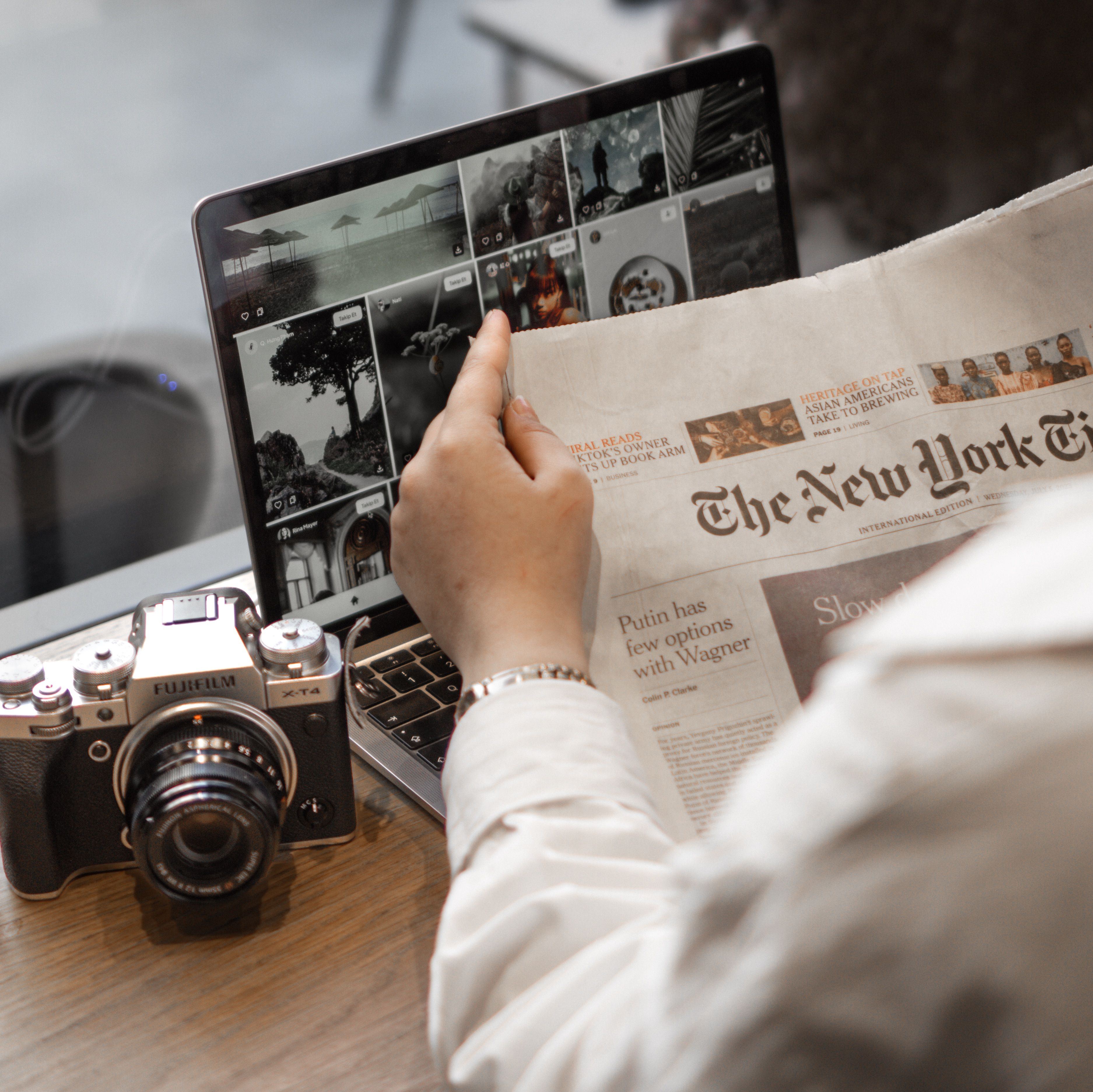 Close-up of a person reading The New York Times beside a laptop and camera