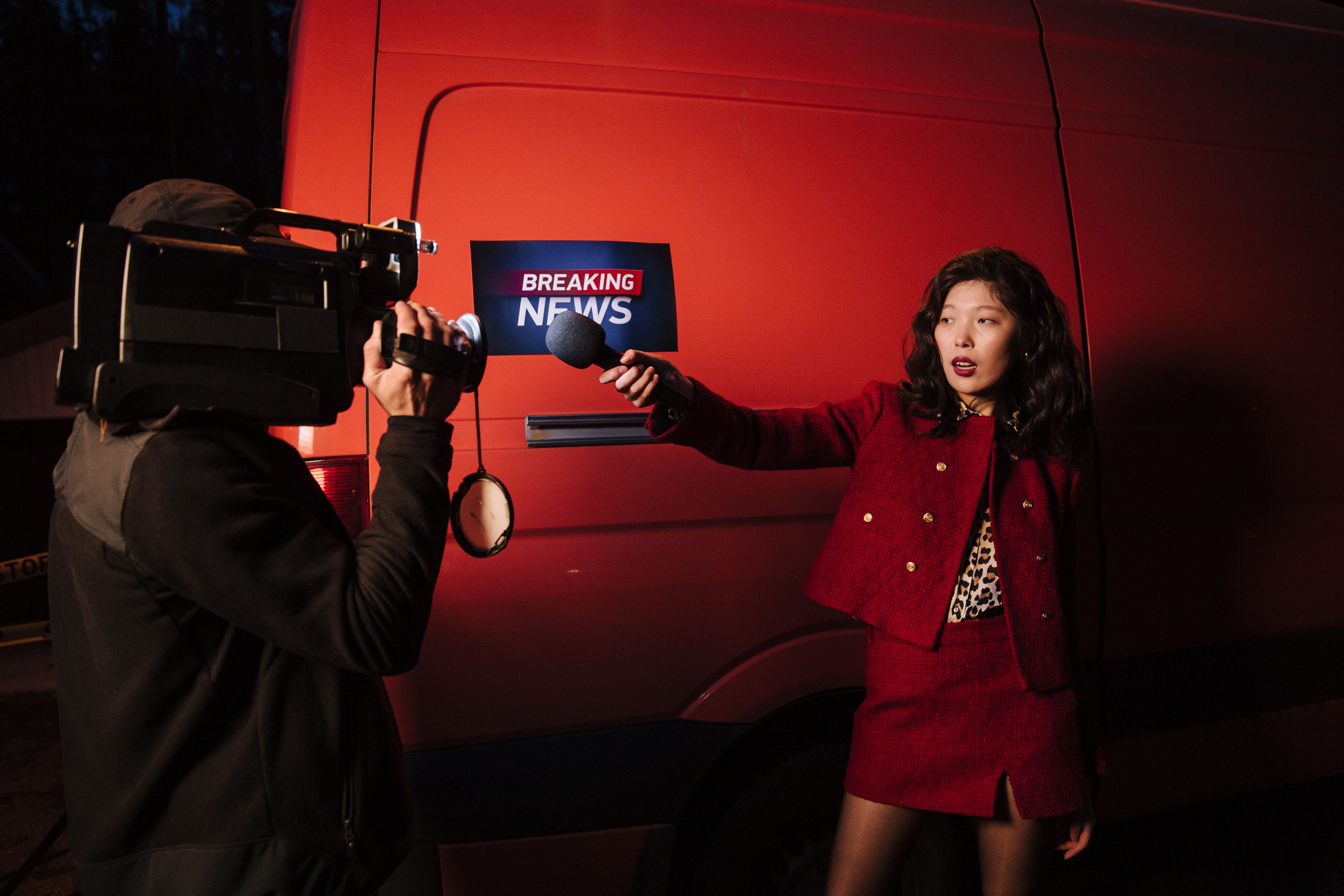 Reporter and cameraman conducting a nighttime news broadcast beside a news van